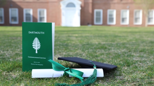 Photo of the 2022 Commencement program, cap, and diploma on the grass outside Baker Library